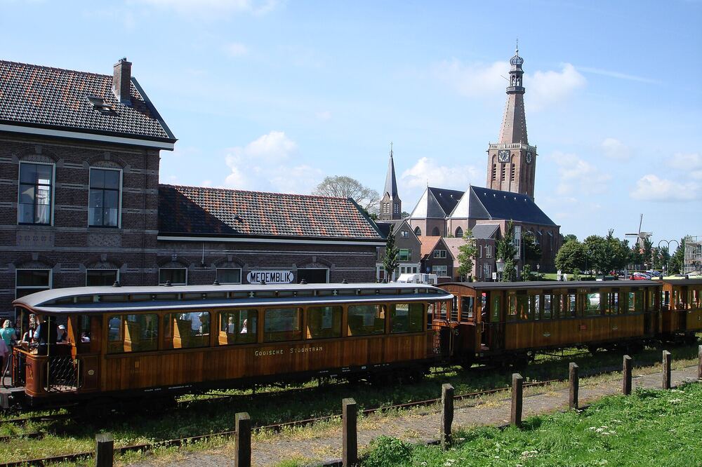 Houten rijtuigen van de museumstoomtram bij station Medemblik, met daarachter de kerktoren en oude huizen